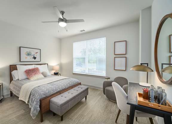 A bedroom with a bed, a chair, a table, and a ceiling fan.