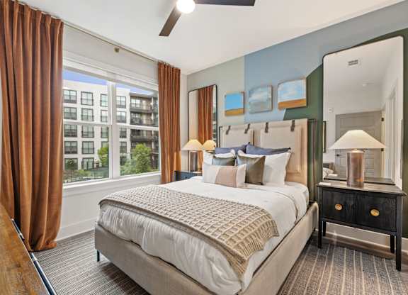 A bedroom with a large bed and a view of a building outside the window.