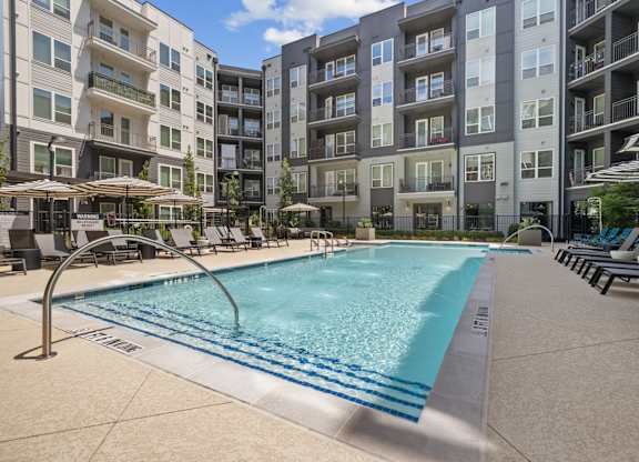 A swimming pool surrounded by apartment buildings and lounge chairs.