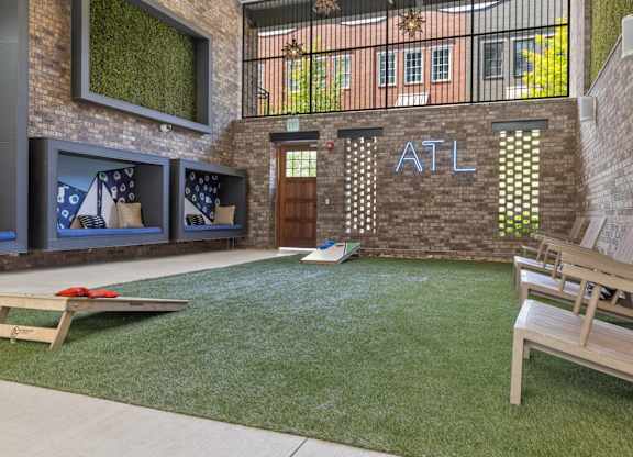 A backyard with a lawn, a bench, and a cornhole game set up.