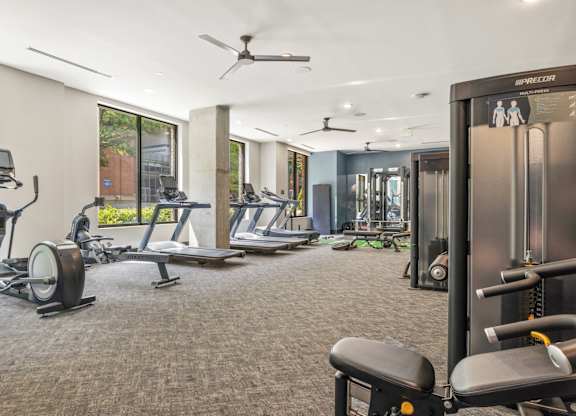 A gym with a variety of equipment including treadmills, weights, and a ceiling fan.