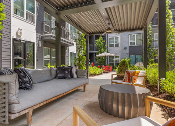 A patio with a grey couch and a round table.