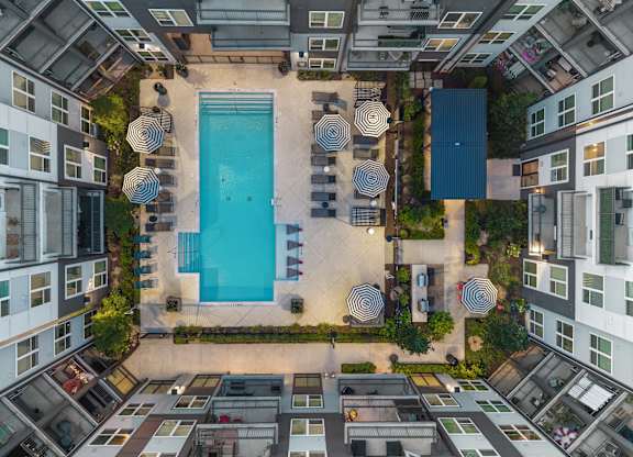 A swimming pool surrounded by lounge chairs and umbrellas in a courtyard.