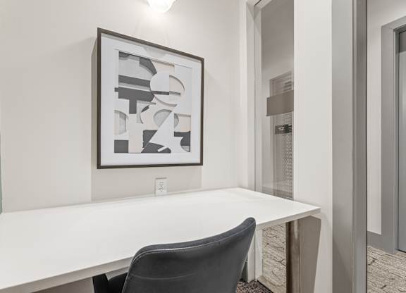 A white desk with a black chair and a framed artwork on the wall.