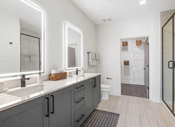 A bathroom with a white sink and grey cabinets.