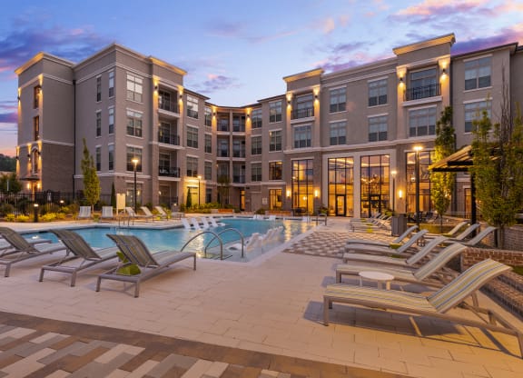 a large swimming pool with chaise lounge chairs and a building in the background