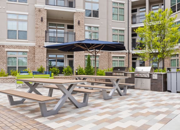 two picnic tables with umbrellas in front of an apartment building