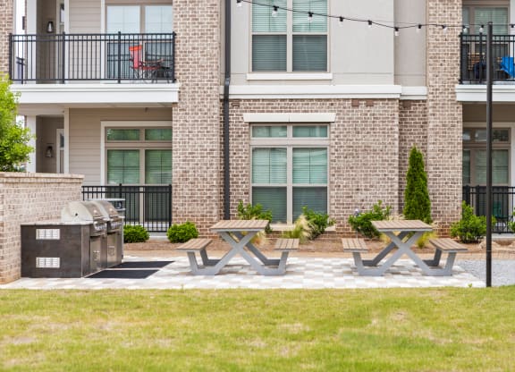 a picnic area with two picnic tables and a grill in front of an apartment building