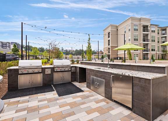 A modern outdoor kitchen area with a grill, sink, and seating area.