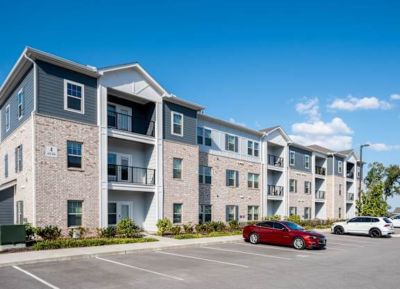A red car is parked in a parking lot in front of apartment buildings.