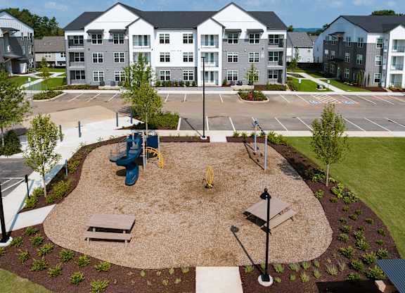 A playground area with a slide, swings, and a bench in front of apartment buildings.