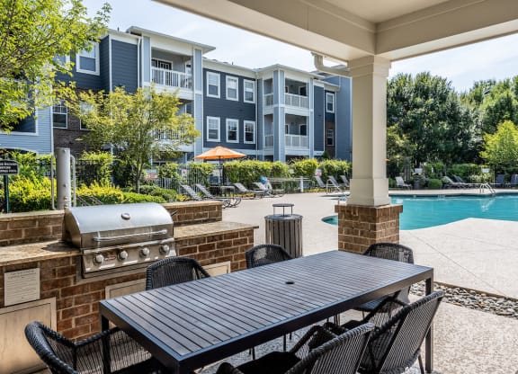 a patio with a grill and table and chairs and a swimming pool in the background