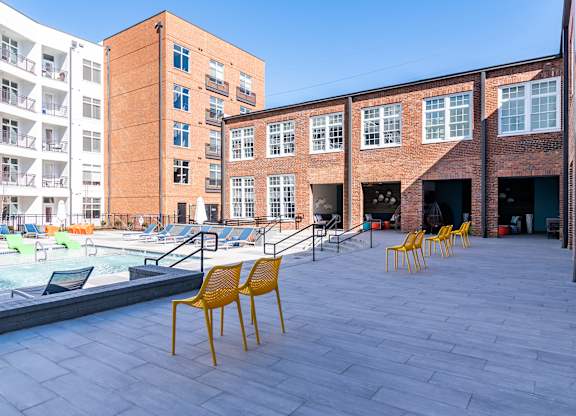 a pool area with yellow chairs in front of a brick building