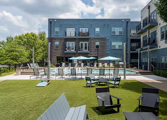 A large grassy area with a pool and chairs in front of a building.