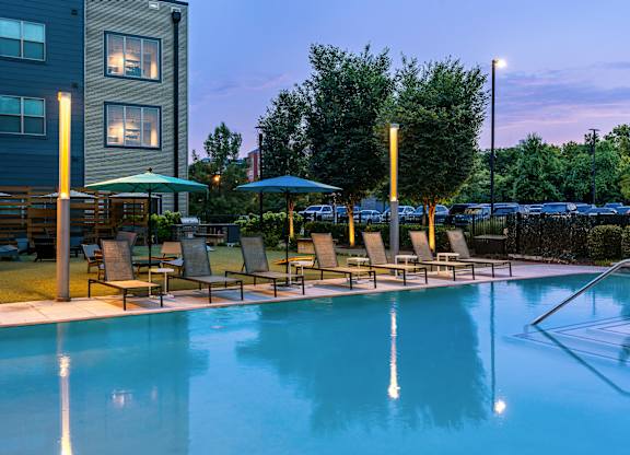 A pool with chairs and umbrellas is lit up at dusk.