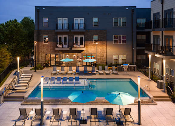 A swimming pool surrounded by chairs and umbrellas in front of a building.