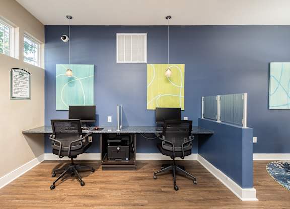 Two black chairs are in front of a desk with a laptop and a monitor.