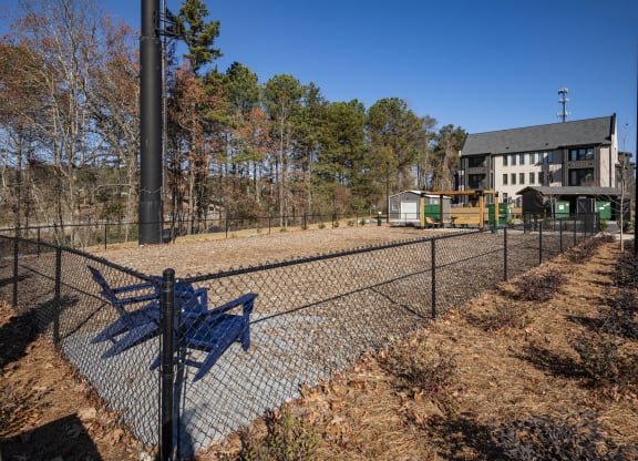 a fenced in dog park with a blue bench and a house in the background