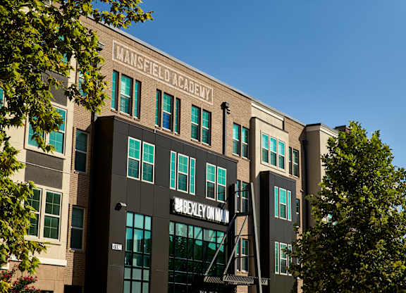 The exterior of the Mansfield Academy building is shown with a clear blue sky in the background.