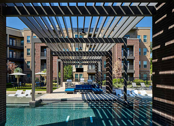 A pool area with a pergola and lounge chairs.