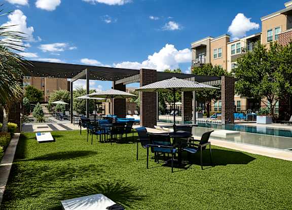 A patio with chairs and umbrellas is surrounded by a grassy area and a pool.