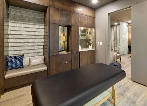 A massage table in a room with wooden cabinets and a window with blinds.