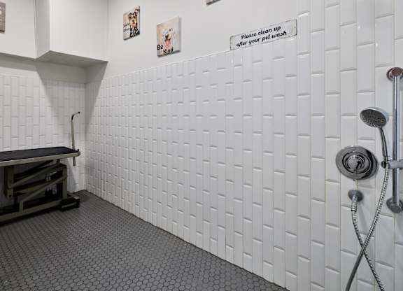 A white tiled bathroom with a shower head and a sign on the wall.