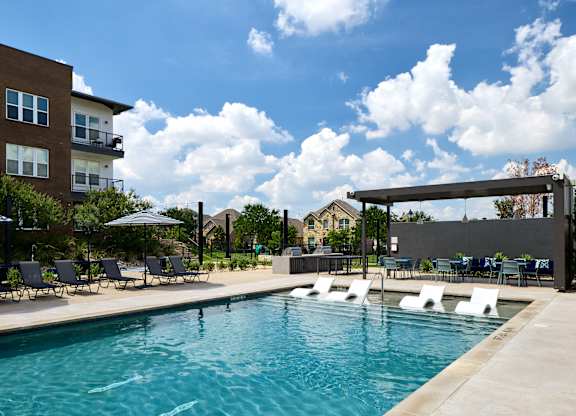 A swimming pool with lounge chairs and umbrellas in front of a building.
