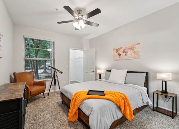 A bedroom with a bed, chair, and a ceiling fan.