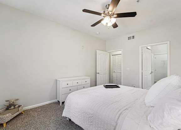 A white bedroom with a bed, dresser, and ceiling fan.
