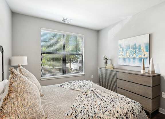 A bedroom with a bed, a nightstand, and a window with blinds.