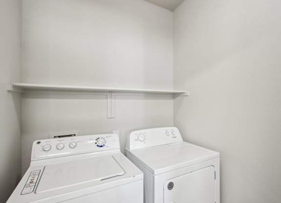 Two white front loading washing machines in a small laundry room at Sweetwater At Metro North Apartments, Phoenix, AZ 85029