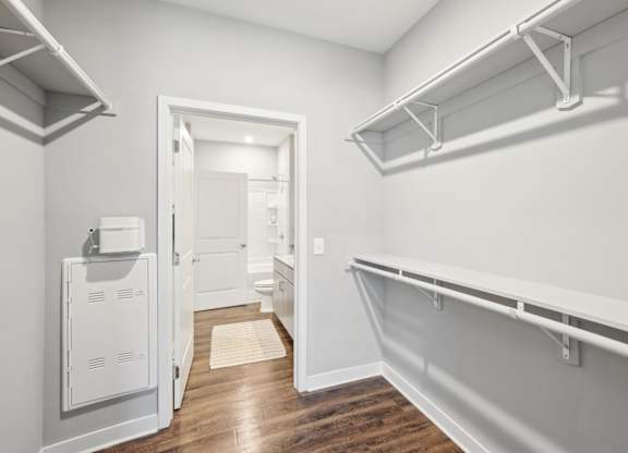 A white walk-in closet with shelves and a doorway leading to a bathroom.