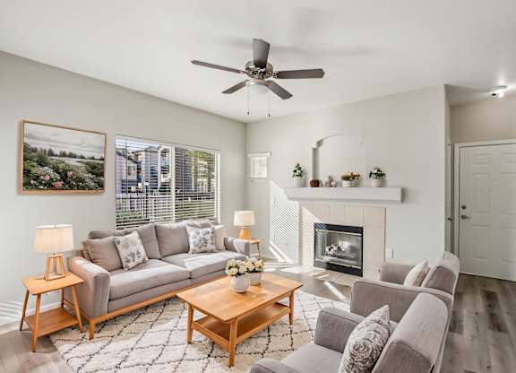 A living room with a grey couch, a coffee table, and a fireplace at Sweetwater At Metro North Apartments, Phoenix