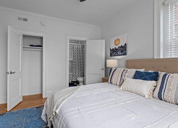A bedroom with a large bed and a window with blinds.