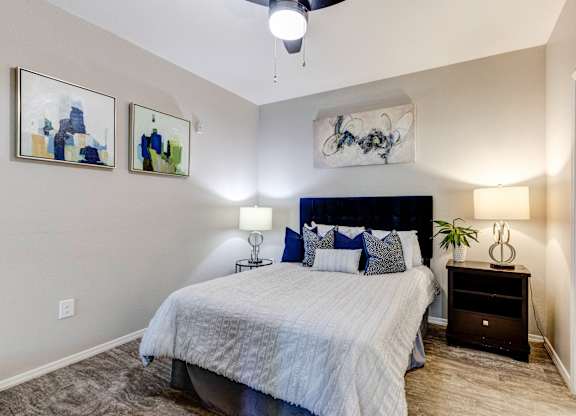 A bedroom with a bed, nightstand, and two wall art pieces at Sweetwater At Metro North Apartments, Phoenix, AZ 85029