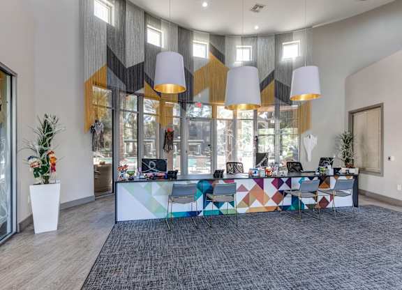 A modern office space with a colorful reception desk and a view of the outside through the glass doors at Sweetwater At Metro North Apartments, Phoenix  85029
