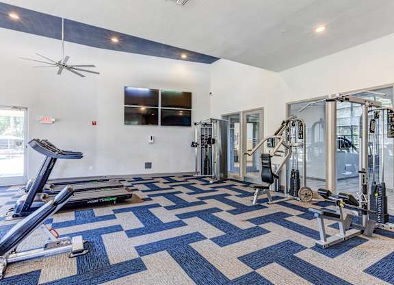 A spacious gym with a variety of equipment and a blue and white patterned carpet at Sweetwater At Metro North Apartments, Phoenix