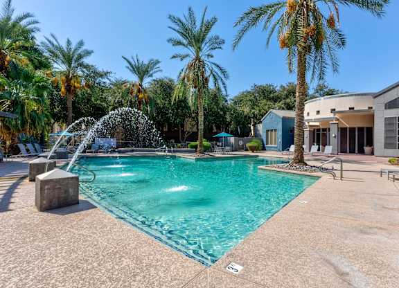 A pool with a waterfall and palm trees in the background at Sweetwater At Metro North Apartments, Arizona 85029