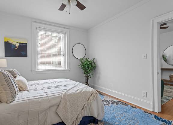A bedroom with a bed, a plant, and a painting on the wall.