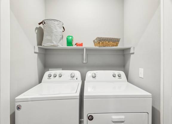 A laundry room with two washing machines and a shelf above them.