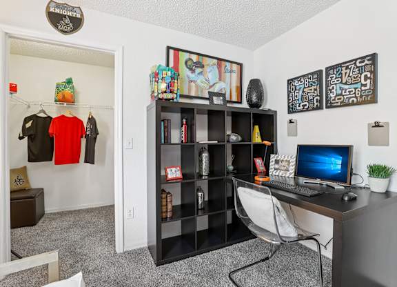 A room with a desk, chair, bookshelf, and a computer monitor.