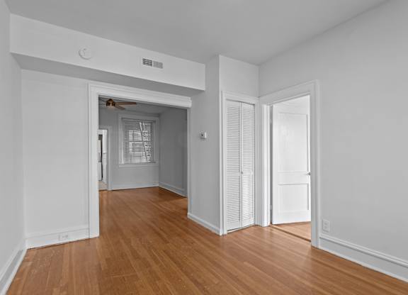 A room with white walls and wooden floors with a doorway leading to another room.