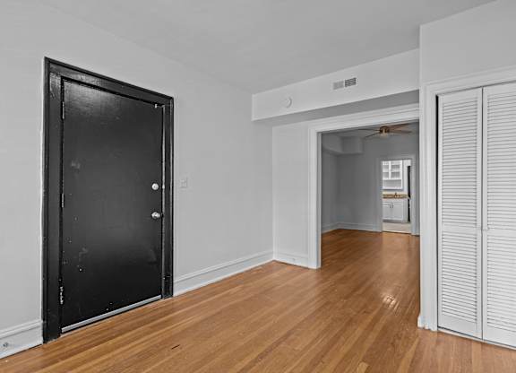 A black door is on the left of a room with a wooden floor and white walls.
