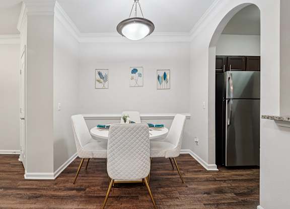 A dining room with a table set for two and a fridge in the corner.