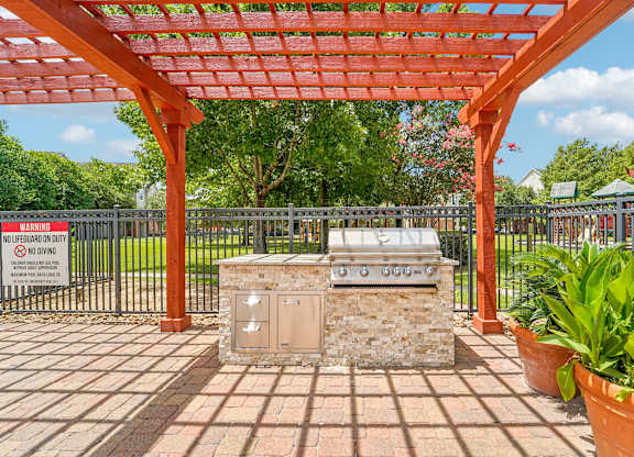 A red pergola is over a stone structure in a park.