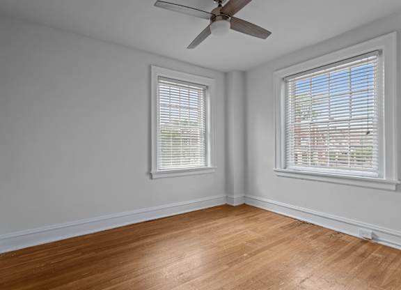A room with a ceiling fan and two windows.
