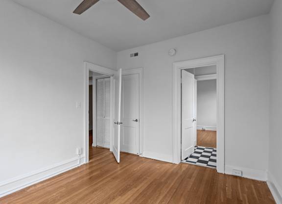 A room with white walls and wooden floors with a ceiling fan.