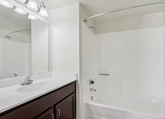 A white bathroom with a sink, mirror, and bathtub.