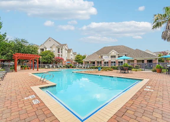 A swimming pool surrounded by a brick patio and lounge chairs.